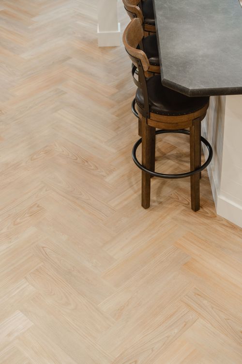 Close-up of light herringbone wood flooring beside a leather-seat barstool