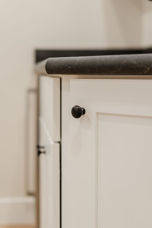 Close-up of a white shaker cabinet with a black knob and dark stone countertop edge