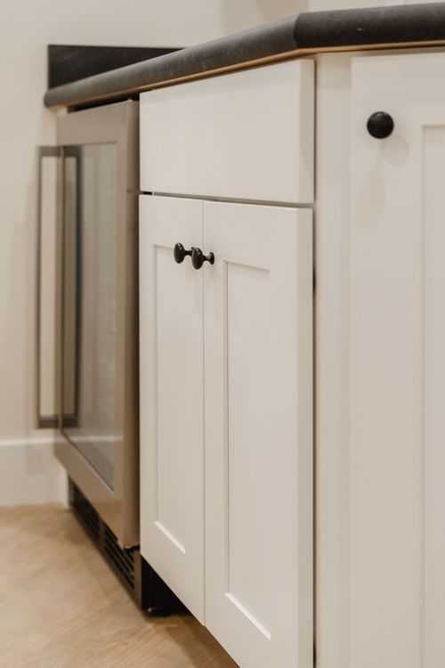 Close-up of white cabinetry with black hardware beside a built-in stainless beverage fridge