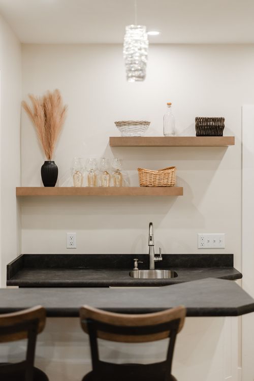 Basement bar with a crystal pendant light, black stone counter and wood barstools