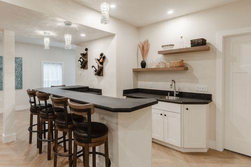 Basement bar with pendant lighting, a wine rack, sink and barstool seating along a black counter