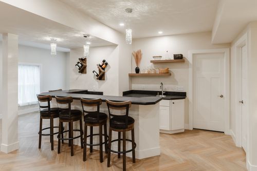 Basement bar with four leather barstools, wall-mounted wine racks and herringbone flooring