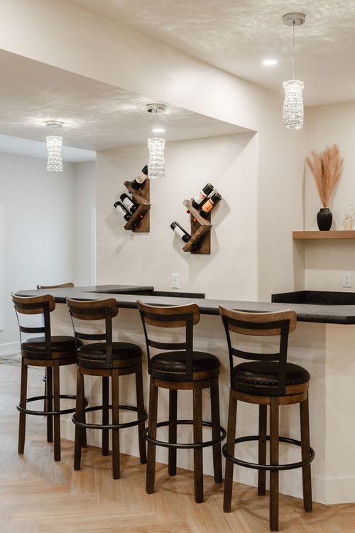 Basement bar seating with four barstools beneath crystal pendant lights and wine racks
