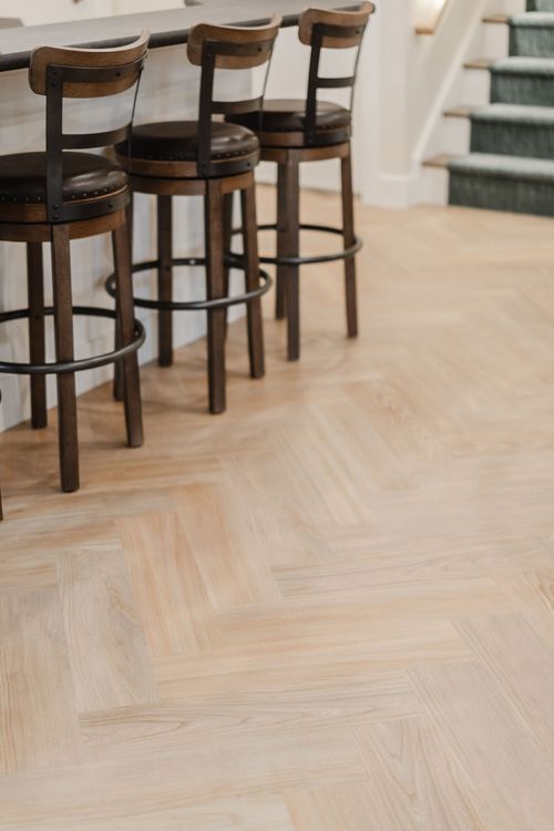 Leather barstools on herringbone flooring beside a staircase with a patterned runner