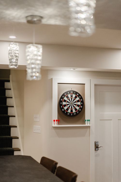 Recessed dartboard cabinet with colorful darts beside a carpeted staircase