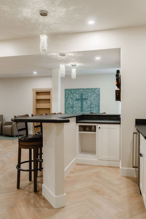 Open basement lounge with a wet bar, pendant lighting and a cozy seating area beyond