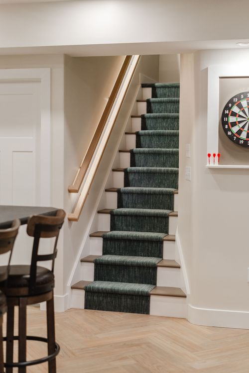 Staircase with a green striped runner and wood handrail lit by integrated LED lighting