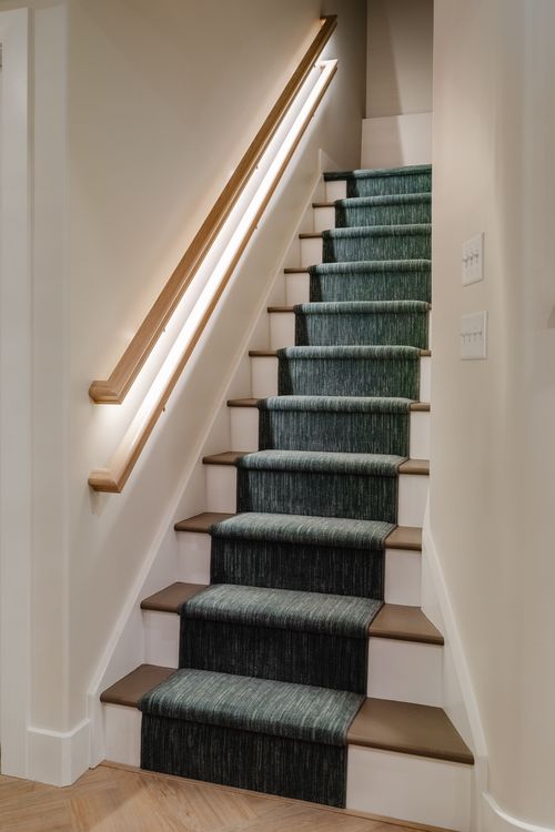 Close view of a staircase with an illuminated wood handrail and green patterned runner