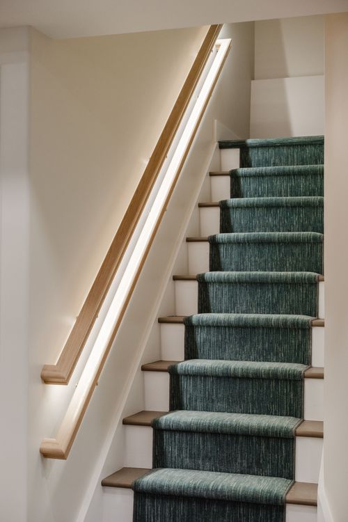 Staircase with a glowing LED handrail descending to a herringbone wood floor