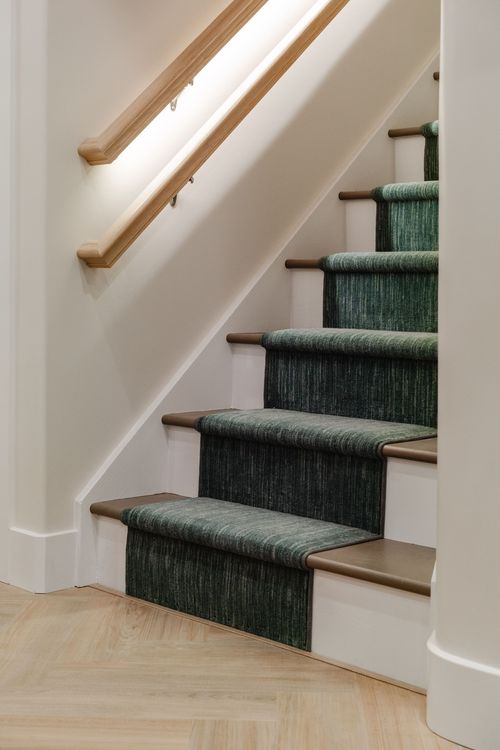 Basement staircase with a backlit wood handrail and green textured stair runner
