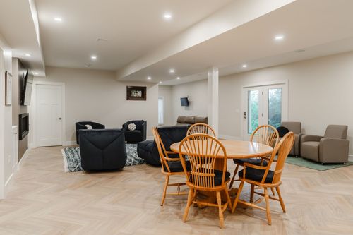 Open basement living and dining area with a wood table, dark sectional and wall-mounted TV