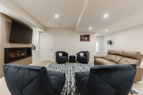 Basement living room with a linear fireplace, wall-mounted TV and navy swivel chairs