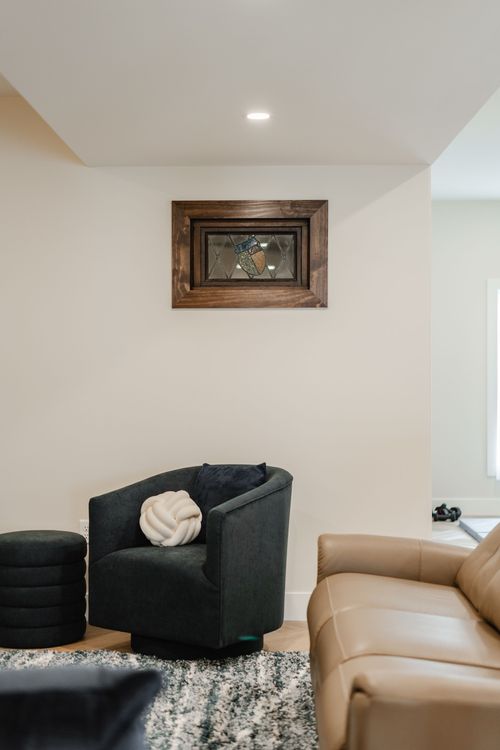 Stained glass wall art above a charcoal swivel chair and tan leather sofa