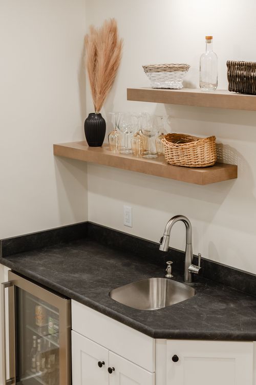 Wet bar with floating wood shelves, wicker baskets, glassware and a stainless prep sink