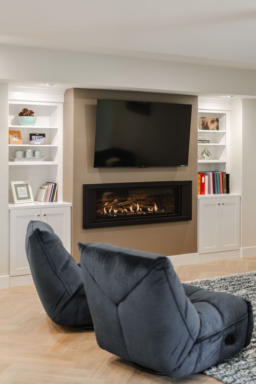 Living area with a linear gas fireplace, wall-mounted TV and built-in white bookshelves