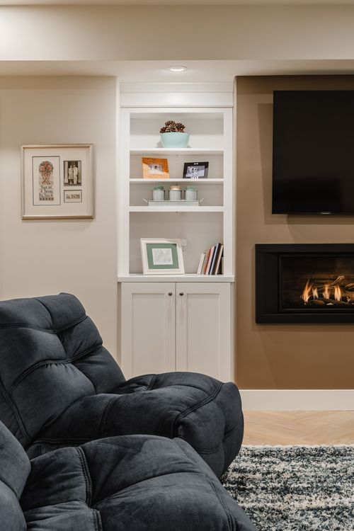 Built-in white bookshelf styled with framed photos, books and decor beside a lit fireplace