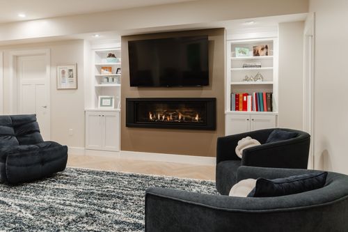 Basement living room with a fireplace, built-in shelving and dark swivel chairs on a patterned rug
