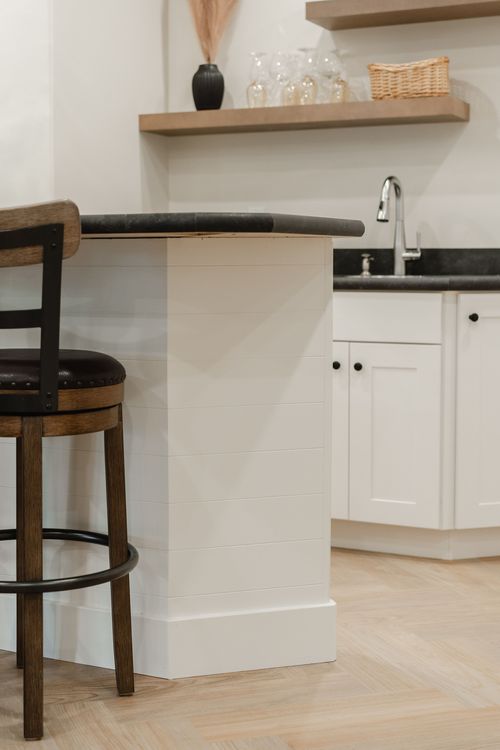 White waterfall-edge bar island with a black soapstone countertop and wood shelving behind