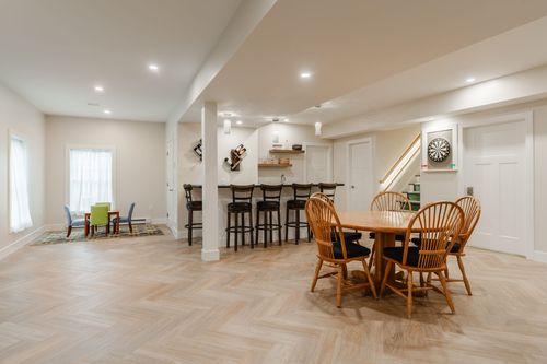 Open basement floor plan with a bar, dining table, play area and herringbone wood flooring