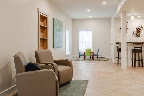 Basement lounge with tan recliners, herringbone flooring and a built-in bar nook