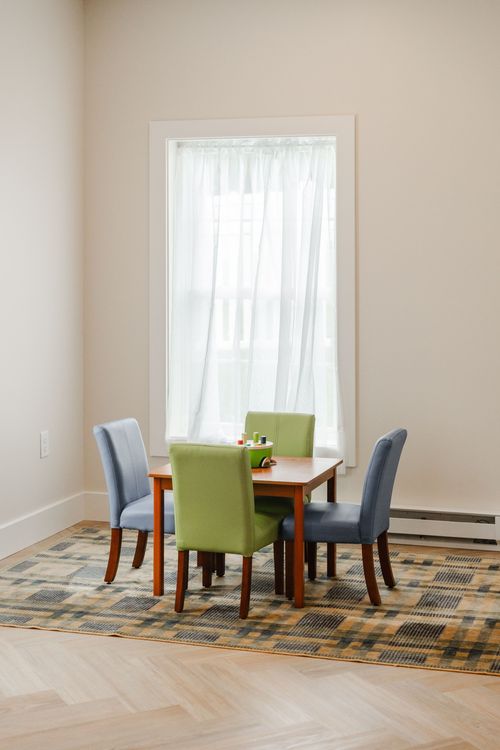Kids activity nook with a wood table, green and blue chairs by a curtained window