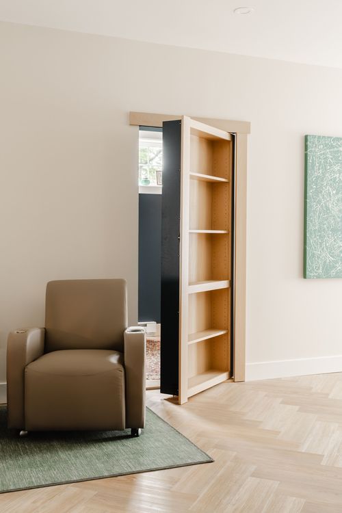 Hidden bookcase door swung open to a dark hallway beyond a leather recliner