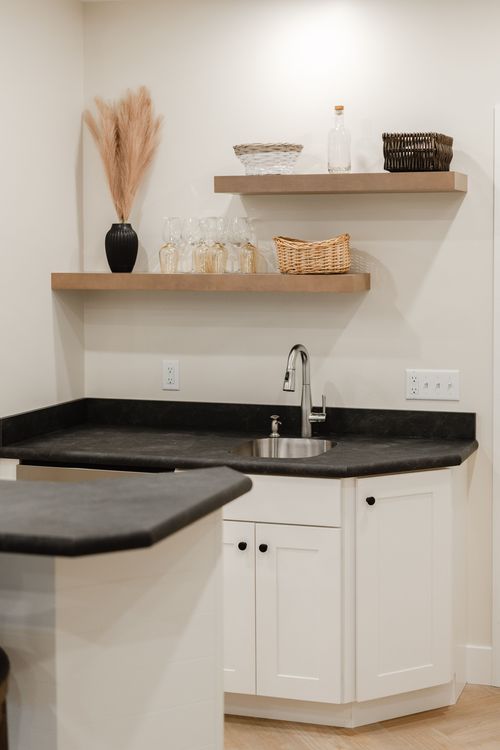 Wet bar corner with floating shelves, a built-in wine fridge and black stone countertop