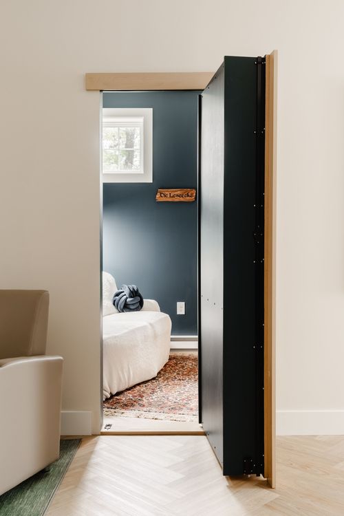 Hidden swinging bookcase door open to a cozy reading nook with a wall sign