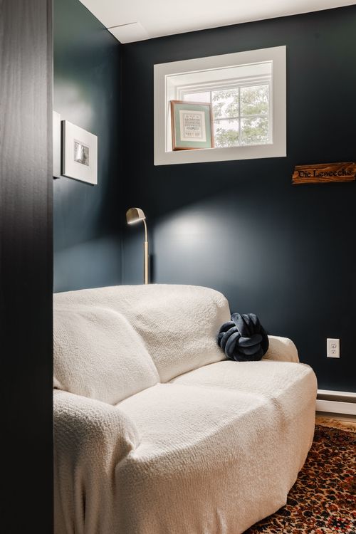 Dark teal reading nook with a boucle sofa, brass floor lamp and framed art