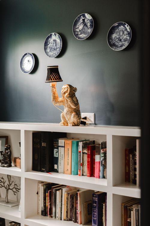 Close-up of a brass monkey-shaped lamp beside a wall of collectible plates
