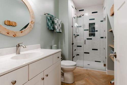 Bathroom with a round burl wood mirror, glass shower and herringbone tile floor