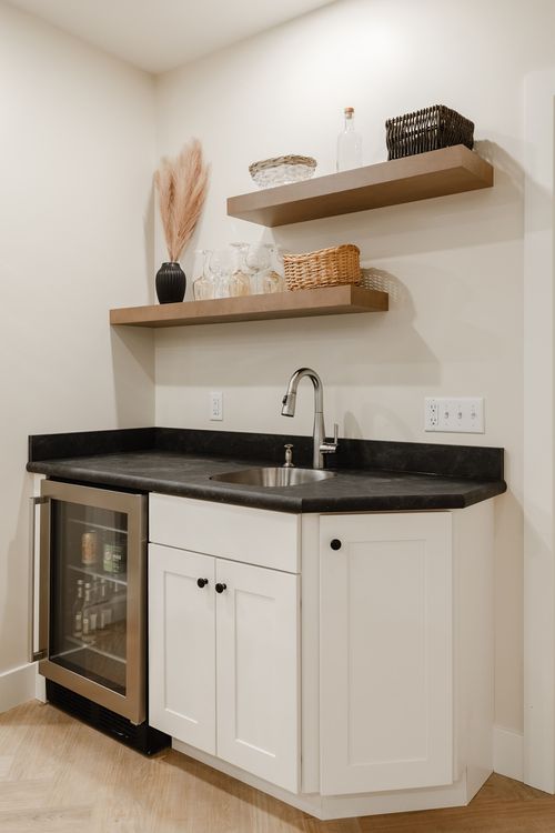 Basement bar nook with open wood shelving, a wine fridge and black stone counters