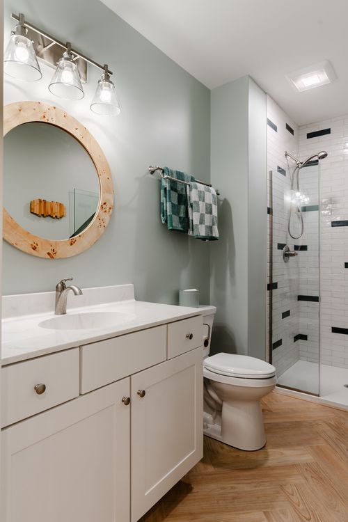 Bathroom with a burl wood mirror, three-light sconce and subway-tiled glass shower