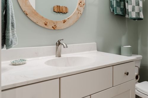Bathroom vanity close-up with a quartz counter, burl mirror and checkered towels