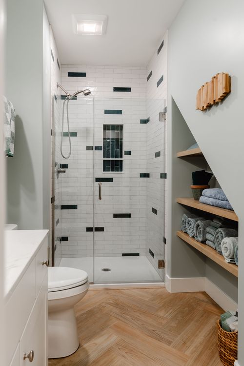 Bathroom shower tucked under the stairs with white subway tile and dark accent tiles