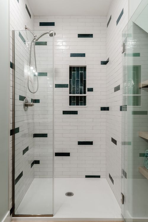 Glass shower stall with white subway tile and a dark green tile niche