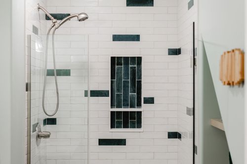Handheld shower head against white subway tile and a green tile niche