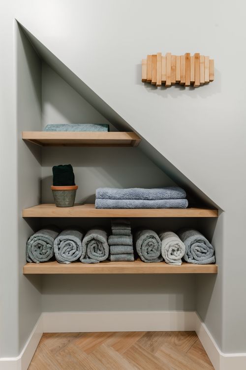 Angled under-stair shelving stacked with rolled towels