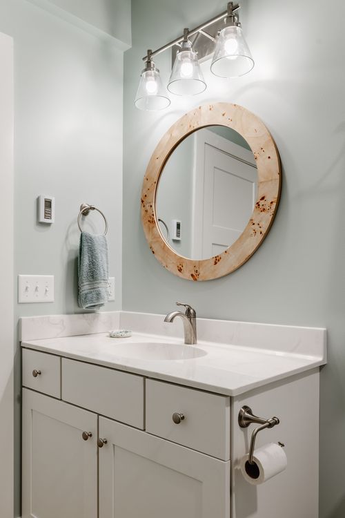 Bathroom vanity with a round burl wood mirror, three-light sconce and mint walls