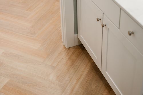 Close-up of herringbone wood flooring meeting a white cabinet base