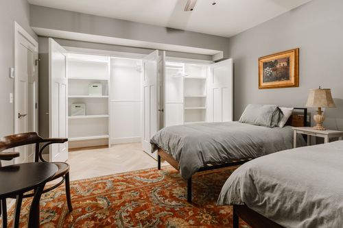 Bedroom with open closets showing storage bins and beds dressed in gray linens
