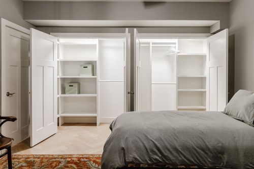 Bedroom with open closets, storage bins and a bed corner in view