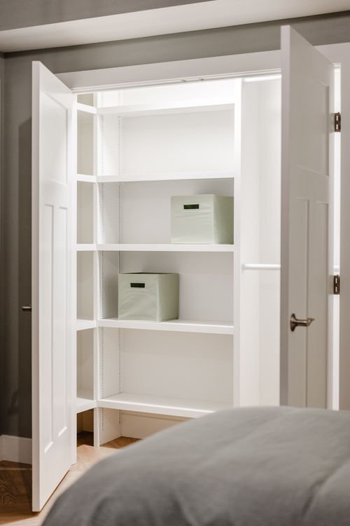 Close-up of an open closet with white shelving and pale green storage bins