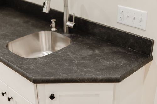 Close-up of a black stone bar countertop with a stainless undermount sink and gooseneck faucet