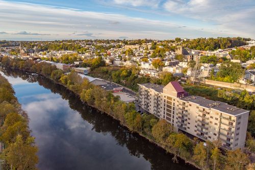 Aerial view of a riverside apartment building with autumn foliage and a town skyline