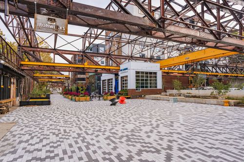 Courtyard with a geometric paver pattern beneath a restored steel trestle