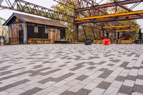 Courtyard pavers leading to a dark wood cabin beneath a steel trestle