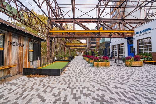 Courtyard walkway with a cornhole board and flower planters under a steel trestle