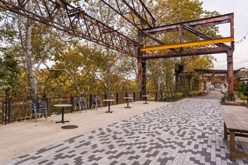 Outdoor seating area with cafe tables beneath a steel trestle canopy