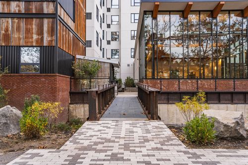 Paver walkway between a corten steel and glass building with landscaping